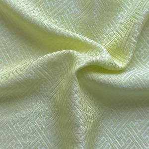 May include: Pale yellow fabric with a white geometric pattern. The fabric is woven with a subtle sheen and has a soft, drapey texture.