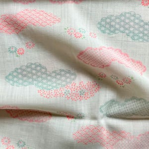 May include: Off-white fabric with a repeating pattern of pink and teal clouds and small floral clusters. The clouds have detailed geometric and scalloped designs. The fabric has a soft, slightly wrinkled texture.