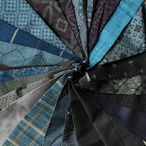 May include: A circular arrangement of fabric swatches in blues, greys, and blacks. The swatches showcase a variety of patterns, such as geometric designs, stripes, and textured weaves. This creates a visually interesting display of textile samples for design purposes.