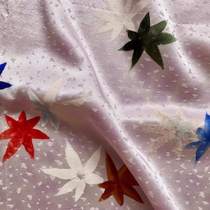 May include: Pale purple fabric with a delicate dotted texture, featuring star-shaped designs in various colours. The stars are blue, red, white, green, and brown, creating a vibrant textile.