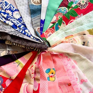 Puede incluir: Una colección de retazos de tela coloridos dispuestos en un patrón circular. Las telas presentan varios patrones, incluidos diseños florales, geométricos y de dibujos animados. Las telas son una mezcla de rosa, azul, verde, rojo y blanco.