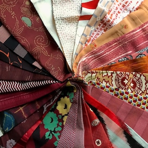 May include: A collection of various fabric swatches arranged in a circular pattern. The fabrics display a range of colors, including burgundy, red, orange, and cream, with diverse patterns such as floral, geometric, and striped designs. The textiles appear to be silk or a similar material.