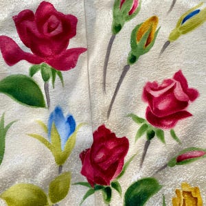 May include: Close-up of a fabric with a floral pattern. The design features watercolor-style red roses, green leaves, and buds in various stages of bloom. The background is a light beige color.