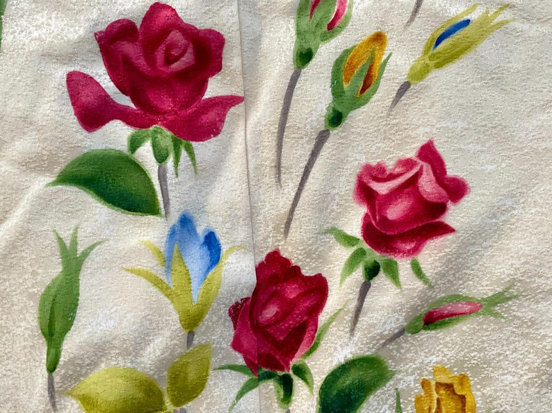 May include: Close-up of a fabric with a floral pattern. The design features watercolor-style red roses, green leaves, and buds in various stages of bloom. The background is a light beige color.