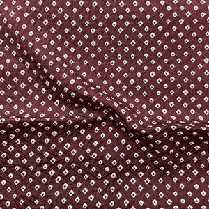 May include: A deep maroon fabric featuring a repeating pattern of small, white, diamond-shaped squares arranged in a grid. The material has a distinct crinkled, textured surface with visible folds and creases that create subtle shadows across the cloth.