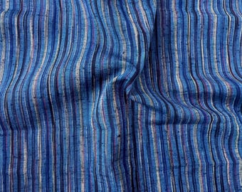 May include: A woven fabric featuring a vertical striped pattern in various shades of blue, including navy, royal, and light blue, interspersed with thin white and dark red lines. The material has a textured surface with small, raised flecks throughout.