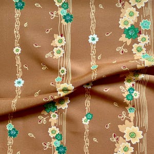 May include: Brown fabric with a floral pattern. Vertical stripes alternate between floral vines and thin lines. The flowers are yellow, green, and white. The fabric has a slight sheen.
