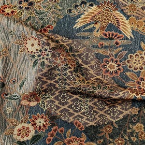 May include: A textile fabric featuring a dark blue background with a repeating pattern of gold and red flowers, stylized cranes, and geometric diamond shapes. The design includes intricate floral motifs and flowing lines in shades of brown, gold, and cream, creating a dense, layered visual texture across the entire surface of the material.
