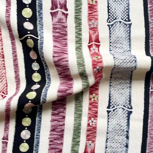 以下が含まれることがあります： さまざまな色合いの縦縞模様の生地のクローズアップ。縞模様には、赤、黒、紫、緑が含まれ、花柄や幾何学模様が施されています。生地は質感があり、クリーム色の背景です。