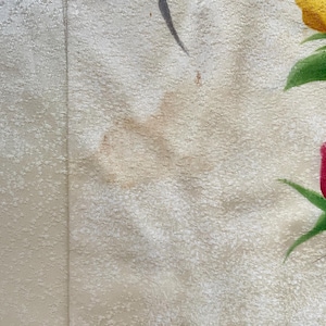 May include: Close-up of a textured, off-white fabric with a vertical seam. The fabric is decorated with painted yellow and red roses with green leaves. The roses are in various stages of bloom.