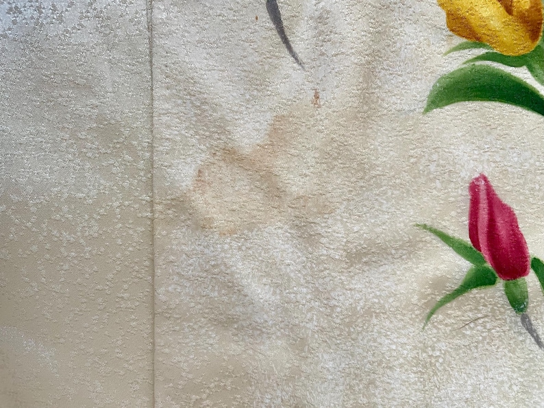 May include: Close-up of a textured, off-white fabric with a vertical seam. The fabric is decorated with painted yellow and red roses with green leaves. The roses are in various stages of bloom.