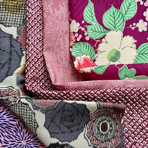 May include: A collection of colorful fabric swatches. The fabrics feature various patterns, including floral designs, geometric shapes, and textured details. Colors include pink, purple, gray, and burgundy.