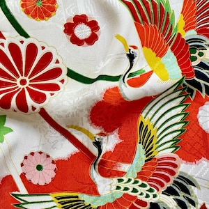 May include: White fabric with a vibrant pattern featuring red, orange, and green cranes, flowers, and decorative elements. The design includes stylized flowers and ribbons, creating a rich, detailed textile.