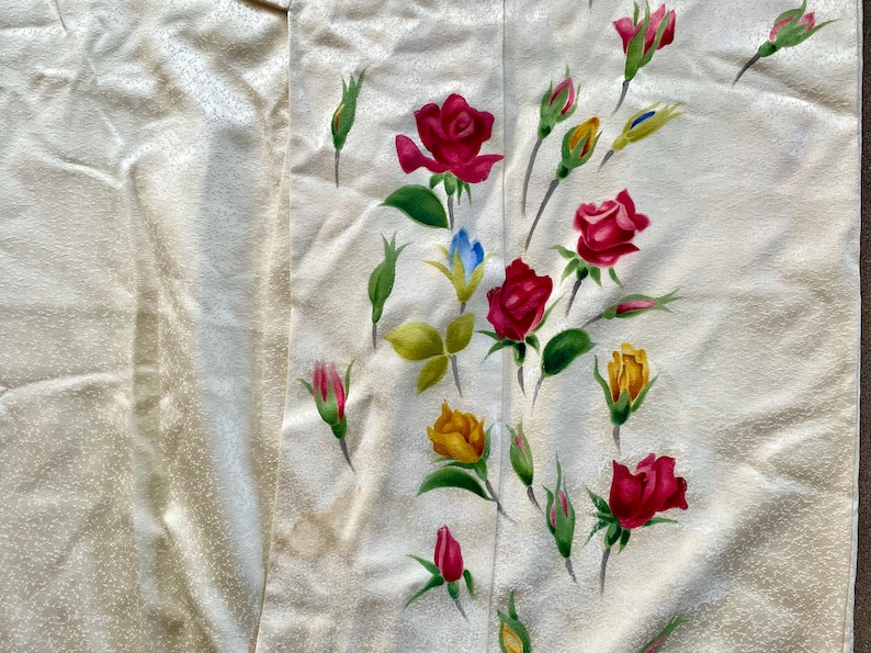 May include: Cream-colored fabric with a floral pattern featuring red, yellow, and pink roses, along with green leaves and buds. The roses are painted in a realistic style, with detailed petals and shading. The fabric has a subtle texture.