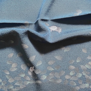 以下が含まれることがあります： 白い葉のような形の模様が入った、質感のある青色の生地のクローズアップ。生地は折りたたまれ、影と奥行きを作り出しています。全体的な効果は柔らかくエレガントで、アパレルや室内装飾に適しています。