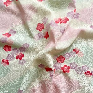 May include: Close-up of a fabric with a floral pattern. The fabric features a repeating design of red and purple flowers, white blossoms, and wavy lines on a light pink and green background. The fabric is soft and flowing.