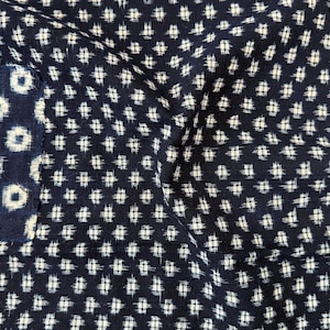 May include: A dark navy blue fabric featuring a repeating white cross-hatch pattern. On the left side, a rectangular patch of fabric is visible, displaying a distinct pattern of white circular rings against a dark navy blue background.
