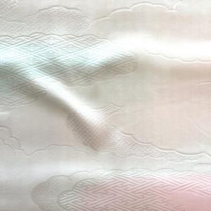 Puede incluir: Una tela blanca con un sutil tejido jacquard tono sobre tono. El textil muestra un patrón repetitivo de nubes estilizadas y formas geométricas de diamante, creando una superficie texturizada con pliegues suaves y fluidos.