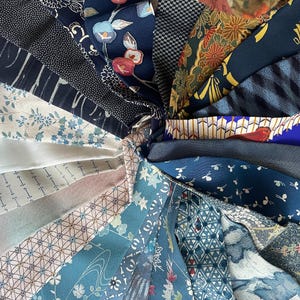 Op de afbeelding: Een verzameling stofstalen in verschillende tinten blauw, wit en bruin. De stoffen hebben verschillende patronen, waaronder bloemen, geometrische en gestreepte ontwerpen.