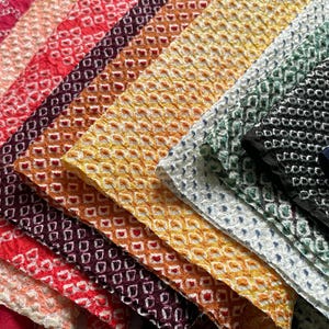 May include: A selection of textured fabrics in a range of colours, including red, orange, yellow, green, and blue. Each fabric features a repeating geometric pattern. The arrangement highlights the different colours and textures of the fabrics, creating a visually appealing display.