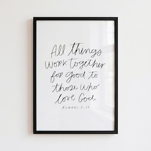 Puede incluir: Un marco rectangular negro que contiene una impresión blanca con texto negro escrito a mano que dice: All things work together for good to those who love God. ROMANS 8:28. El diseño presenta una estética simple, limpia y de alto contraste.