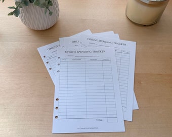 Puede incluir: Varias hojas de papel blanco con el texto "ONLINE SPENDING TRACKER" apiladas sobre una superficie de madera clara. Cada hoja tiene una cuadrícula para el seguimiento de gastos, con columnas para fecha, descripción, categoría e importe. Un macetero blanco y una vela en el fondo.