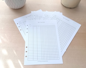 May include: Several white paper bill tracker sheets with a grid layout and the text "BILL TRACKER" are fanned out on a light wood surface. The sheets have pre-punched holes for binders. A white ceramic vase and a glass jar are in the background.