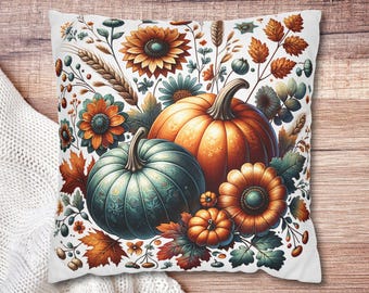 May include: White square pillow featuring a fall-themed design. The design includes two orange pumpkins, a teal pumpkin, and various flowers and leaves in shades of orange, teal, and brown. The pillow is placed on a wooden surface.