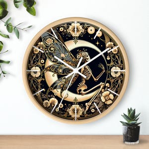 Puede incluir: Un reloj de pared redondo con marco de madera clara. La esfera del reloj presenta un hada esqueleto con alas detalladas, sentada en una luna creciente sobre un fondo negro, rodeada de diseños florales.