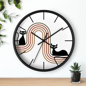 May include: A black and white wall clock with a retro design featuring two black cats sitting on a rainbow-colored arch. The clock has black hands and a black frame.