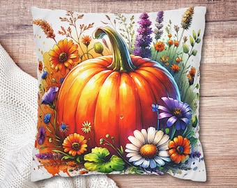 May include: A decorative pillow featuring a vibrant orange pumpkin surrounded by colorful flowers and foliage. The pillow has a white background and is set against a wooden surface, perfect for fall decor.