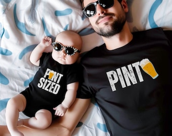 May include: A black onesie with the text "PINT SIZED" and a beer graphic, worn by a baby, next to a person wearing a black t-shirt with the word "PINT" and a beer graphic. Both are wearing sunglasses.