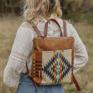 May include: A brown and tan backpack with a geometric pattern on the front pocket. The backpack has brown leather straps and a top handle. The bag is made of canvas and leather.