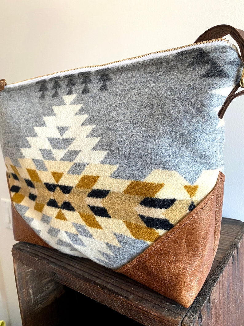 Puede incluir: Un bolso tote de patr&oacute;n geom&eacute;trico gris y marr&oacute;n con fondo de cuero y cierre de cremallera.