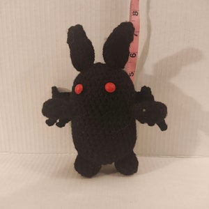 May include: A black crocheted plush toy shaped like a rabbit with red button eyes.