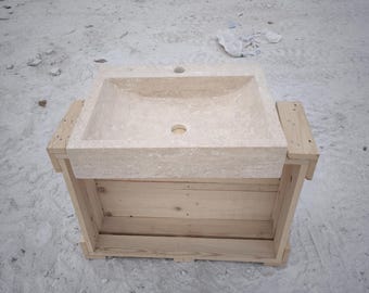 May include: A rectangular, beige stone sink with two circular drain holes, set within a light-colored wooden crate. The sink has a textured surface and a simple, modern design. The wooden crate is constructed from planks of wood.