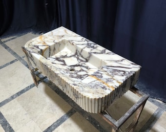 May include: A white marble sink with a rippled edge and a rectangular shape. The sink is on a metal stand.