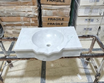 Könnte beinhalten: Ein weißes Marmor-Waschbecken mit einer abgerundeten Schüssel und einem einzigen Abflussloch. Das Waschbecken steht auf einem Holzrahmen.