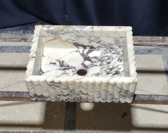 May include: A white marble sink with a wavy edge and a black and white marbled pattern. The sink has a round drain hole in the center.