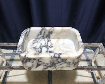 May include: A white marble sink with a rectangular shape and a swirling pattern of purple and brown veins. The sink is sitting on a metal stand.