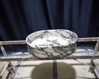Könnte beinhalten: Ovaler Marmorsteinwaschbecken mit einem weißen und grauen Marmormuster. Das Waschbecken ruht auf einem Metallständer.