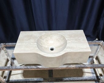 May include: A beige travertine stone bathroom sink with a curved design and a single drain hole. The sink is on a wooden stand.