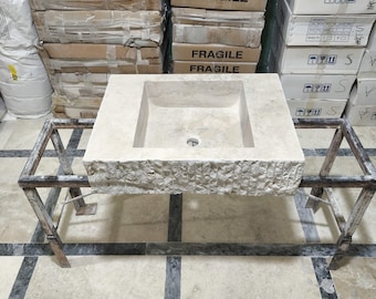 May include: A rectangular stone sink with a square basin, sitting on a metal stand. The sink is made of a light beige stone with a textured surface. The stand is made of black metal and has a simple design.