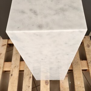 K&ouml;nnte beinhalten: Ein wei&szlig;er Marmorsockel mit einer glatten, polierten Oberfl&auml;che. Der Sockel ist rechteckig und steht auf einer Holzpalette.