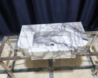 May include: A white marble bathroom sink with purple veining. The sink is mounted on a wooden frame.