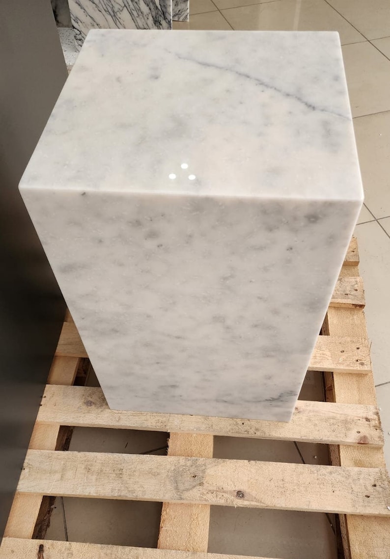 K&ouml;nnte beinhalten: Ein wei&szlig;er Marmor-W&uuml;rfelsockel, der auf einer Holzpalette steht.