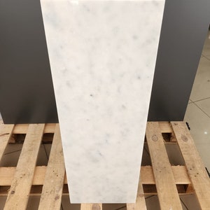 K&ouml;nnte beinhalten: Ein wei&szlig;er Marmorsockel mit einer glatten, polierten Oberfl&auml;che. Der Sockel steht auf einer Holzpalette.