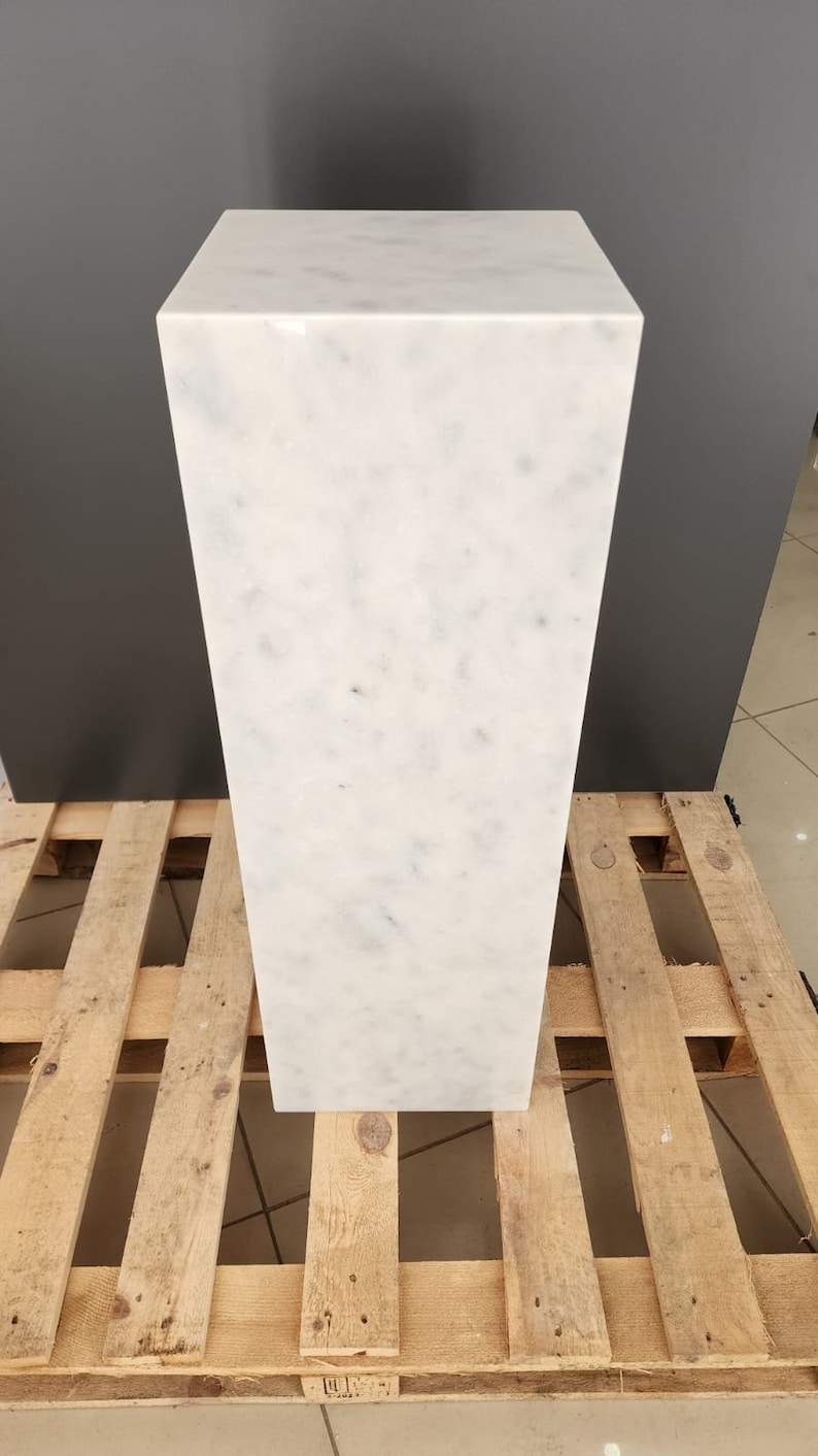 K&ouml;nnte beinhalten: Ein wei&szlig;er Marmorsockel mit einer glatten, polierten Oberfl&auml;che. Der Sockel steht auf einer Holzpalette.