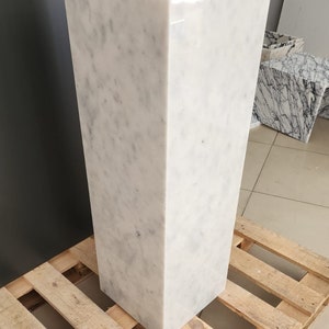 K&ouml;nnte beinhalten: Ein wei&szlig;er Marmorsockel mit einer glatten, polierten Oberfl&auml;che. Der Sockel steht auf einer Holzpalette.