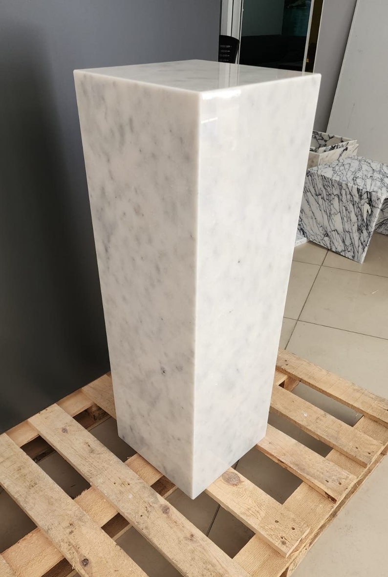 K&ouml;nnte beinhalten: Ein wei&szlig;er Marmorsockel mit einer glatten, polierten Oberfl&auml;che. Der Sockel steht auf einer Holzpalette.